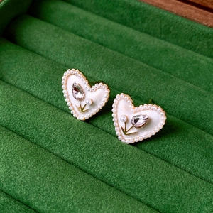 Detail of golden heart stud earring with pearl and tulip carving on green velvet