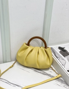 Detail of yellow pleated cloud bag featuring retro circular wooden handle and chain strap