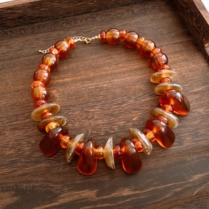 Macro view of amber acrylic irregular beads and teardrop pendant on a wooden tray