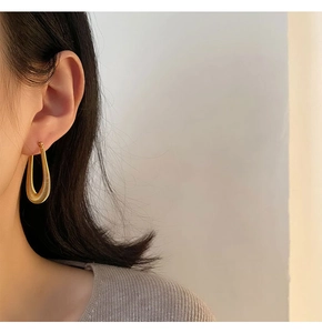 Close-up of gold U-shaped horseshoe textured earrings worn on female ear for detail