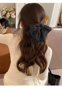 Close-up of a large French style black polka dot chiffon bow hair clip on wavy hair