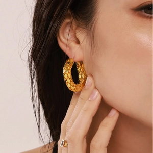 Chunky gold-plated hoop earrings with textured scale pattern on a model