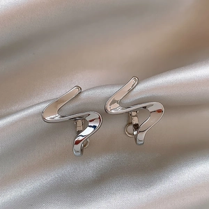 Detailed view of silver polished wave earrings on soft champagne satin fabric background