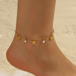 Detail of gold butterfly and pearl charms on an anklet worn on a sandy beach setting