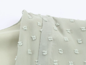 Gros plan sur le tissu mousseline vert clair à pois suisses et les détails de couture d'épaule