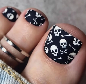 Macro shot of press-on toenails featuring black and white skull and crossbones designs