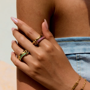 Close-up of gold titanium rings with green and pink zircons and a MAMA charm bracelet