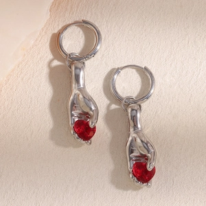 Vintage silver hand design earrings with red heart gemstone on beige paper background