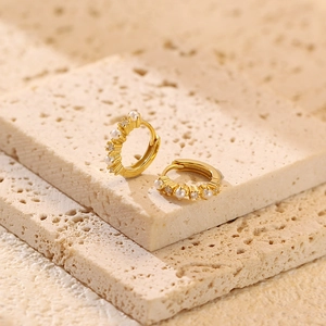 Close-up of gold-plated hoop earrings featuring small pearls and sparkling zircons