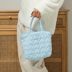 Detail of light blue quilted heart handbag showing soft puffy texture and carry handles