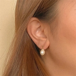 Elegant gold drop earrings with white teardrop pearls worn on female model side profile