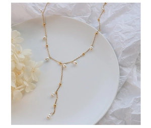 Detail of elegant Y-shaped gold necklace featuring small white pearls and glossy gold beads