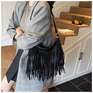 Detail view of black leather shoulder bag with tassels and adjustable strap shown on model