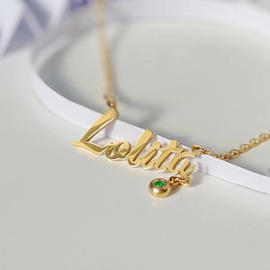 Macro shot of custom gold name necklace Lolita with a green gemstone and cross chain