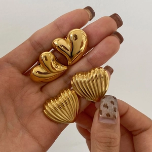 Detail of gold heart earrings in polished and textured finishes held by hand
