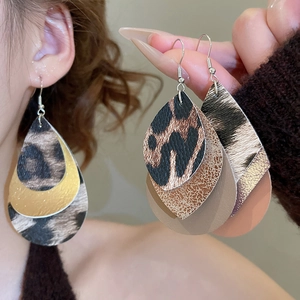Detail of teardrop leopard print leather earrings featuring metallic layered leaf charms