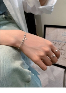 Detail of silver fish charm bracelet and pearl rings on a woman wearing white shirt