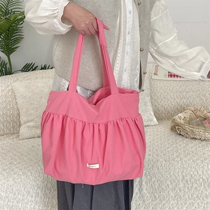 Detailed view of pink pleated canvas tote bag with side ties on a soft textured sofa