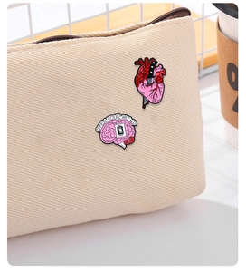 Close-up of enamel heart with dagger and pink brain pins pinned on a beige canvas bag