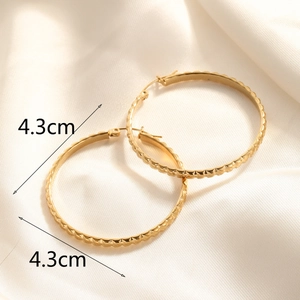 Detail view of 4.3cm gold hoop earrings with diamond-cut texture on satin background