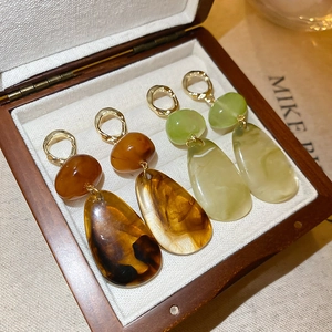 Detailed macro view of irregular resin drop earrings in amber and olive green with gold accents