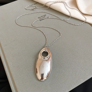 Macro shot of large silver oval hollow pendant on textured book with soft silk fabric