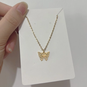 Gros plan d'un pendentif papillon doré ajouré sur une fine chaîne en acier doré