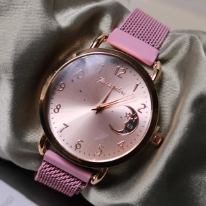 Macro detail of a rose gold quartz watch with moon design on green silk fabric