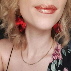 Detailed view of elegant red rose petal earrings worn with a gold chain necklace