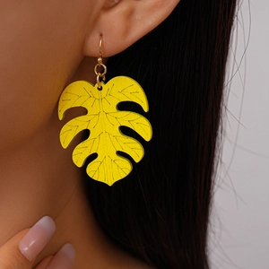 Close-up of yellow leaf dangle earrings with black vein details on a female model