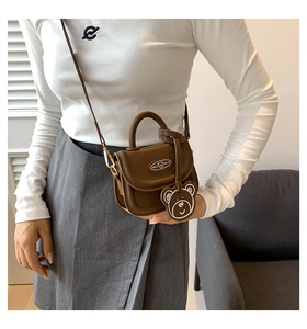 Mini brown crossbody saddle bag with bear charm and adjustable strap worn by a model