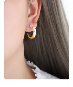 Close-up of C-shaped bamboo earrings with gold metal and white enamel for women