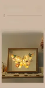 Detailed close-up of DIY shell art butterfly inside wood frame with warm LED lighting
