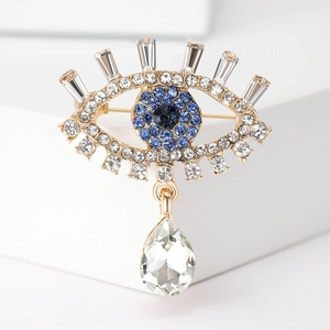 Detailed macro view of the golden Evil Eye brooch with blue crystals and teardrop pendant