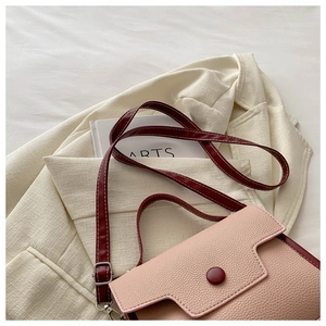 Close-up of pink and burgundy litchi grain leather shoulder bag on white blazer