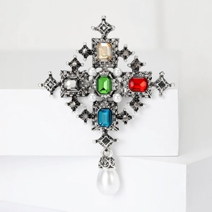 Baroque cross brooch with colorful gemstones and hanging pearl on a white background