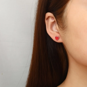 Minimalist red heart stud earrings with silver borders shown on ear model