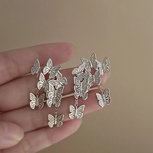 Detailed view of layered silver butterfly drop earrings held in hand for scale