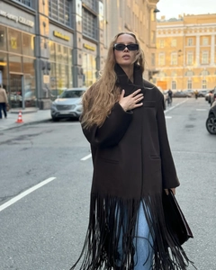 Close-up of a dark brown oversized woolen coat featuring long fringe tassels at the hemline