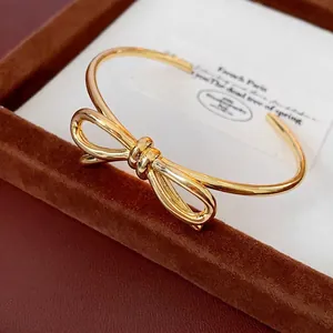 Elegante bracciale rigido dorato a forma di fiocco presentato in una scatola di velluto