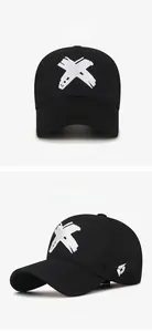Detail view of cotton baseball cap with white X embroidery and wing logo on black fabric