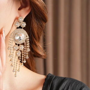 Dettaglio di orecchini vintage dorati con nappe e strass indossati da una modella