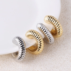 Twisted C-shaped hoop earrings in gold and silver finish on a textured beige surface
