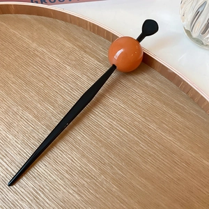 Close-up of a minimalist black hair stick featuring a vibrant orange sphere on top