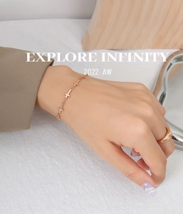Detail of rose gold minimalist cross chain bracelet and polished ring worn by a model