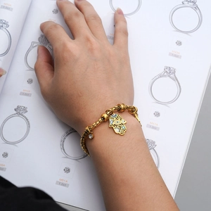 Gouden Hamsa-armband met blauw Evil Eye-bedeltje gedragen over een catalogus