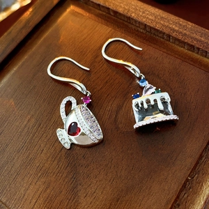 Detailed shot of asymmetrical silver earrings with coffee cup and cake charms on wood
