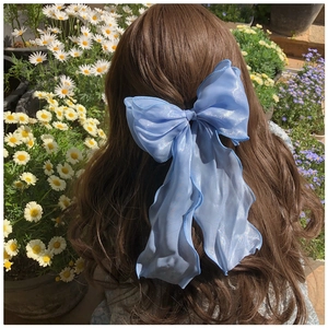 Macro detail of large blue organza bow hair clip with streamers on wavy brown hair