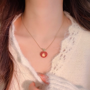 Close-up of a delicate apple pendant necklace with red resin and golden beads.