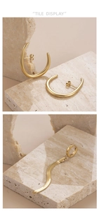 Detail of gold C-shape hoop earrings and snake chain tassel earrings on marble